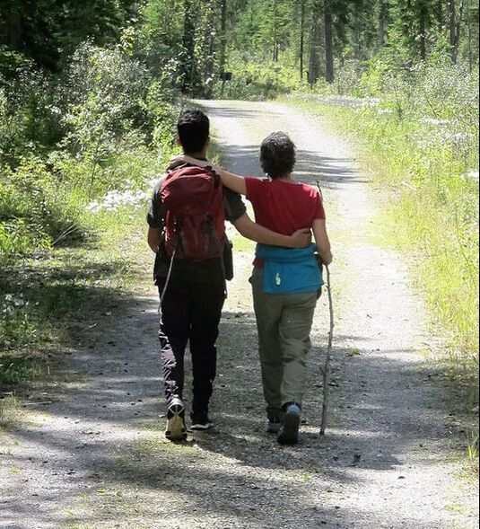 Two people walking side by side on a forest trail.